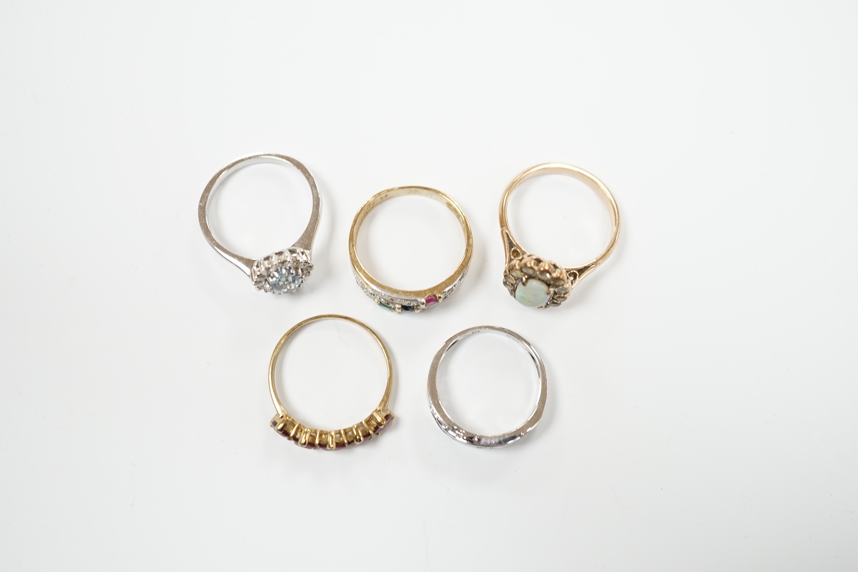 Four assorted 9ct and gem set rings, including opal and white sapphire?, blue topaz and diamond, sapphire and diamond chip crossover and five stone garnet? and a yellow metal and four colour cubic zirconia ring, gross we